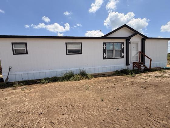 A white manufactured home with black window trim, finished with white skirting across the front.