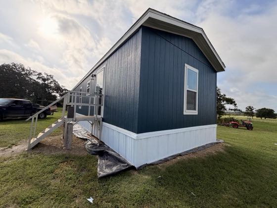 A navy blue home with white skirting and a metal access ramp at the entry.