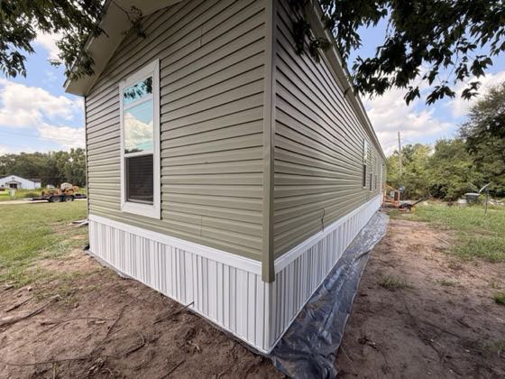 The corner of a sage green vinyl home finished with white skirting.