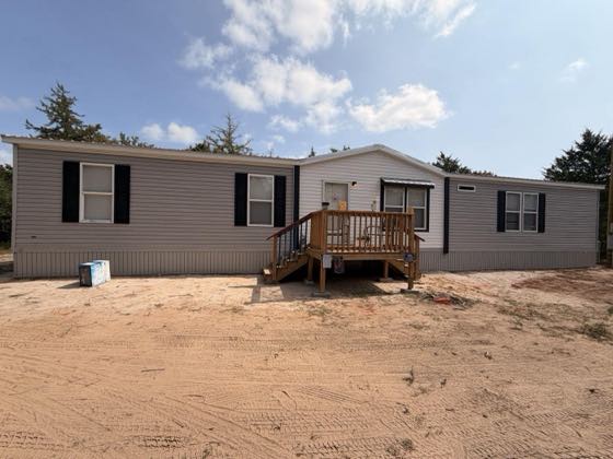 The front of a tan home with a wooden deck and stair, skirted across the full front.