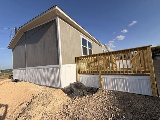 A grey home with a wooden deck, finished with white skirting over a gravel bed.